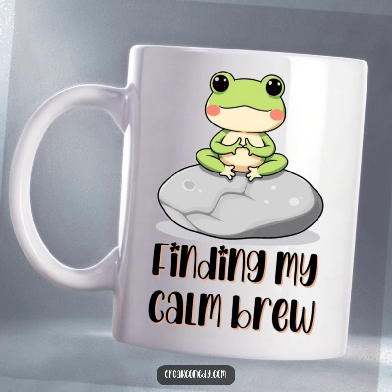 Funny mug depicting a meditating frog character sitting peacefully on a smooth grey stone, radiating calm.