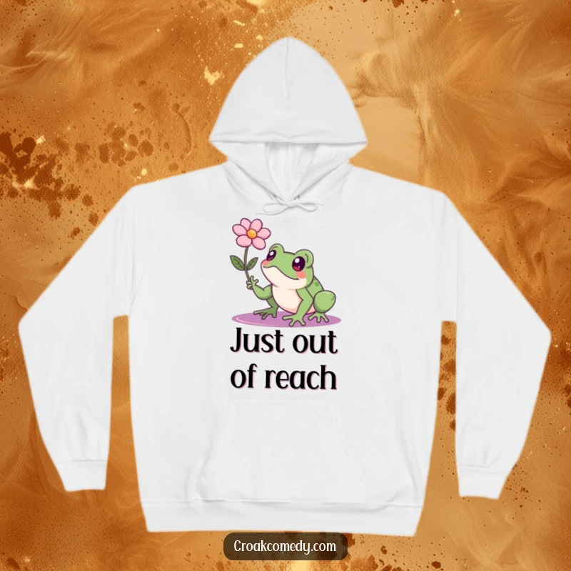 Funny frog with a resolute expression reaching for a floating flower, a comfortable hoodie for dreamers and go-getters.