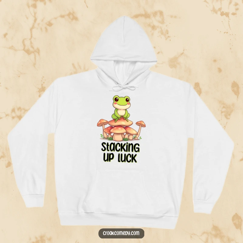Funny Frog Hoodie: A happy cartoon frog balancing on a pile of mushrooms, a comfy and humorous representation of equilibrium.